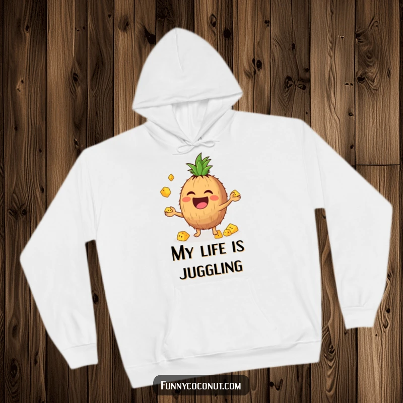 Funny hoodie with a laughing coconut character enthusiastically juggling small pineapple chunks, radiating joy and warmth.